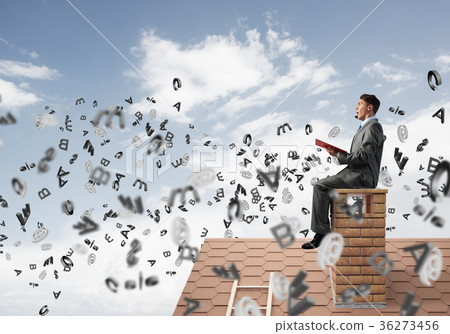 Man on brick roof reading book and symbols flying around 36273456