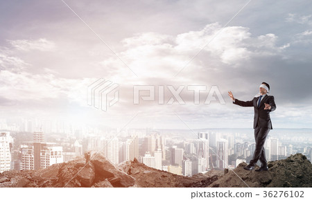 Young businessman in blindfold walking carefully and cityscape at background 36276102