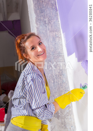 woman paints wall with purple paint roller 36280841