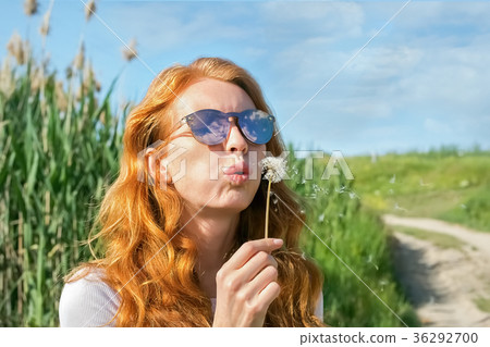 red-haired girl in sunglasses blows away dandelion 36292700