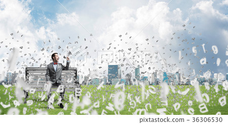 Businessman in summer park on bench announcing something in loudspeaker and symbols fly around Businessman in summer park on bench announcing something in loudspeaker and symbols fly around 36306530