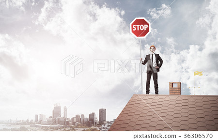 Caucasian businessman on brick house roof showing stop road sign Caucasian businessman on brick house roof showing stop road sign 36306570