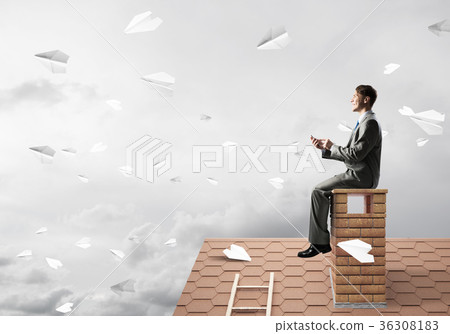 Man on brick roof send message with smartphone and paper planes flying in air Man on brick roof send message with smartphone and paper planes flying in air 36308183