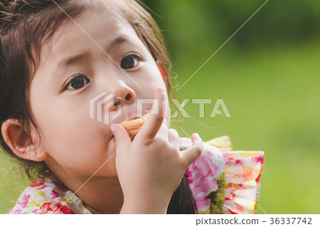 Portrait a Cute Little Asian Girl Eating cookie on Green Nature Portrait a Cute Little Asian Girl Eating cookie on Green Nature 36337742