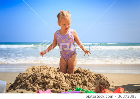Blonde Girl Stands on Wet Sand Heap on Sea Beach 36372385