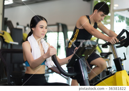 Attractive young woman and young man biking in gym Attractive young woman and young man biking in gym 36381822