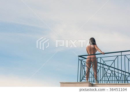 Naked female with camera on balcony opposite sky  36451104