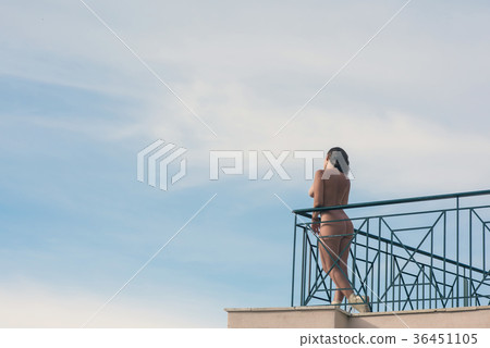 Naked female with camera on balcony opposite sky Naked female with camera on balcony opposite sky 36451105