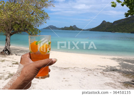 Hand holding a glass of orange juice on the beach 36458135