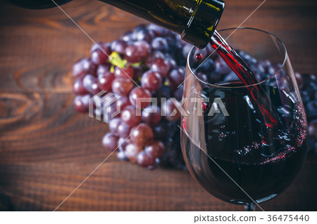 Pouring red wine into the glass with a bunch red Pouring red wine into the glass with a bunch red 36475440