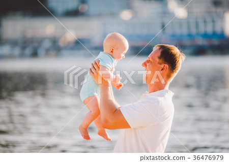 A young father holds one year of his son in arms 36476979