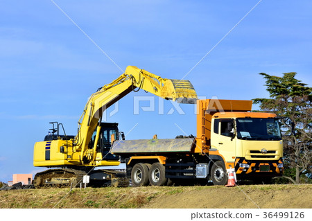 A hydraulic excavator loading asphalt rubble into a dump truck 36499126