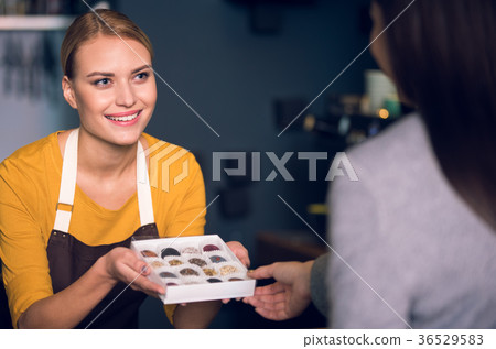 Cheerful seller demonstrating candies to client Cheerful seller demonstrating candies to client 36529583
