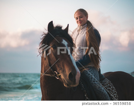 blonde woman sitting on black horse at sea beach 36559858