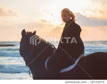 woman sitting on black horse at sea beach 36559870