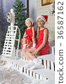 Mom and daughter in Christmas costumes are sitting under snow 36587162