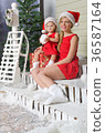 Mom and daughter in Santa's suits are sitting under snow 36587164