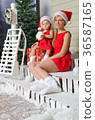 happy mom and daughter in Santa's suits are sitting under snow 36587165