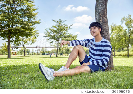 Young guy take a relax in park, sit on green grass and walking in around. 091 36596076