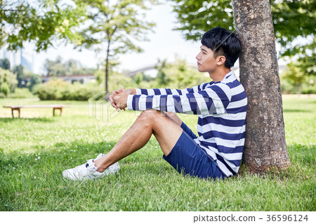 Young guy take a relax in park, sit on green grass and walking in around. 117 36596124