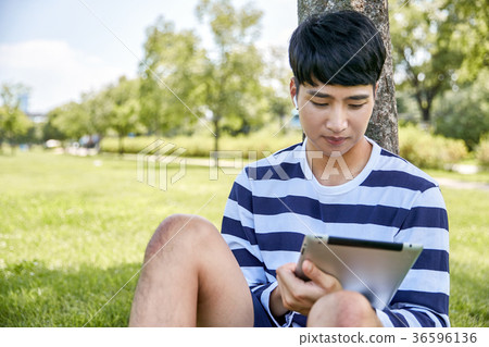 Young guy take a relax in park, sit on green grass and walking in around. 119 36596136