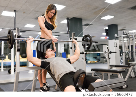 Personal trainer helping a young man lift weights Personal trainer helping a young man lift weights 36603472
