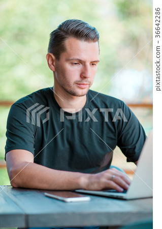 Young man with laptop in outdoor cafe drinking Young man with laptop in outdoor cafe drinking 36642286
