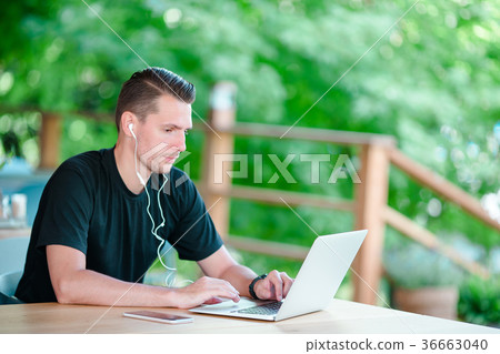 Young man with laptop in outdoor cafe drinking Young man with laptop in outdoor cafe drinking 36663040