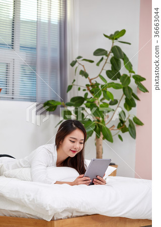 Twenties woman lying on bed and doing iPad Twenties woman lying on bed and doing iPad 36663044