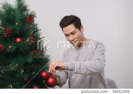 Asian man standing by new christmas tree at home 36682066