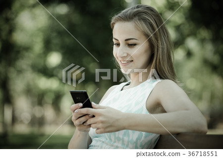 girl sitting on a bench and using phone in park 36718551
