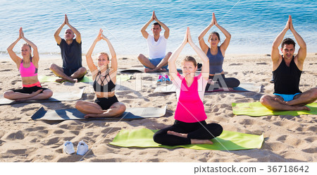 Sporty people practicing yoga on beach Sporty people practicing yoga on beach 36718642
