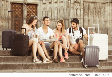 four glad traveling young people searching for direction using paper map in European town four glad traveling young people searching for direction using paper map in European town 36719006
