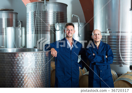 Two happy men in uniforms standing in winery fermentation compartment 36720317