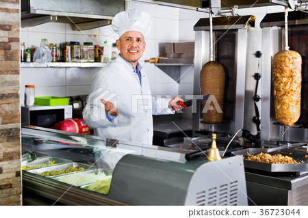 Cheerful mature man cook cutting kebab meat on kitchen Cheerful mature man cook cutting kebab meat on kitchen 36723044
