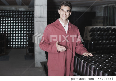 Man winery working in aging section with bottle racks in cellar Man winery working in aging section with bottle racks in cellar 36724731