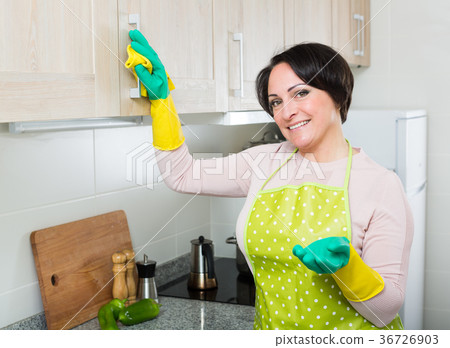 Middle aged woman dusting furniture in kitchen Middle aged woman dusting furniture in kitchen 36726903