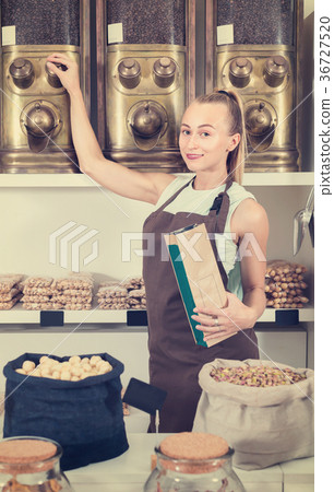 Portrait of girl seller who is standing near showcase with nuts in alimentacion store. 36727520