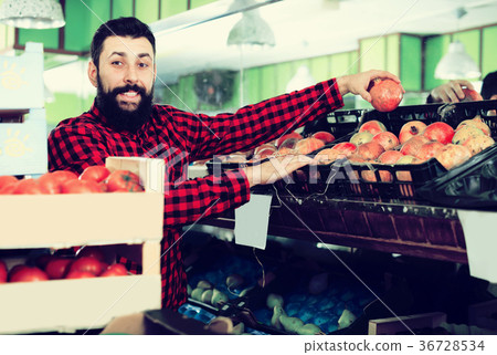 Male seller offering pomegranates in shop 36728534
