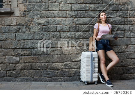 Smiling young woman with travelling bag on stone wall background Smiling young woman with travelling bag on stone wall background 36730368