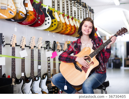 Girl buyer is deciding on acoustic guitar 36730405