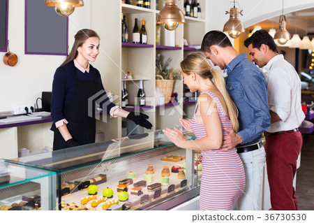Positive waitress is offering delicious cakes from showcase Positive waitress is offering delicious cakes from showcase 36730530