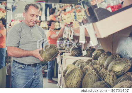 Smiling male is choosing green melon in the supermarket. 36731407