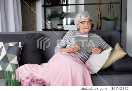 Elderly pensive lady relaxing on couch with book Elderly pensive lady relaxing on couch with book 36742572