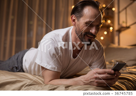 Cheerful mature male using mobile phone at home Cheerful mature male using mobile phone at home 36745785