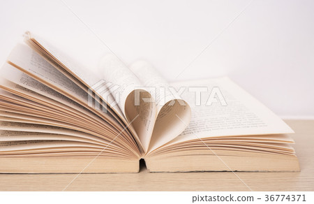 Page of book curved into heart shape on wood table 36774371