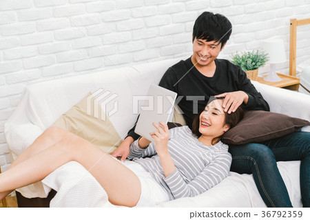 Asian couple relaxing on sofa at home using tablet 36792359