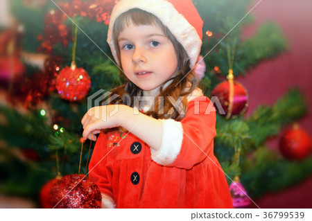 Little girl in Santa's dress by the Christmas tree Little girl in Santa's dress by the Christmas tree 36799539