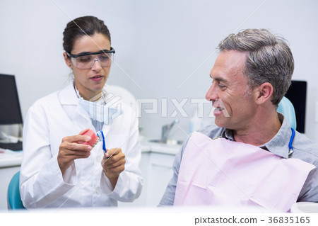 Dentist teaching man brushing teeth on dental mold 36835165