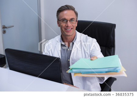 Portrait of dentist holding file while sitting by computer 36835375